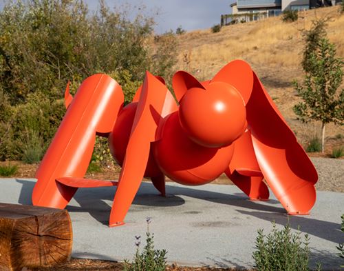Arachnicat, orange-red metal art sculpture located at Clover Park